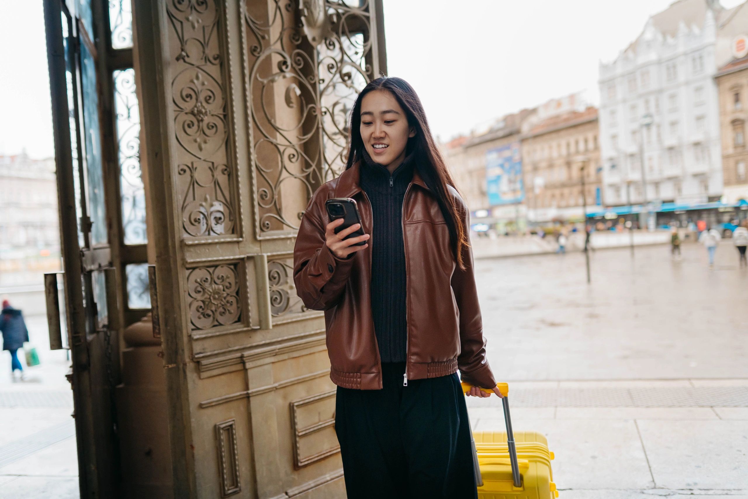 Young Woman Using Smartphone While Traveling With Yellow Suitcase Outdoors